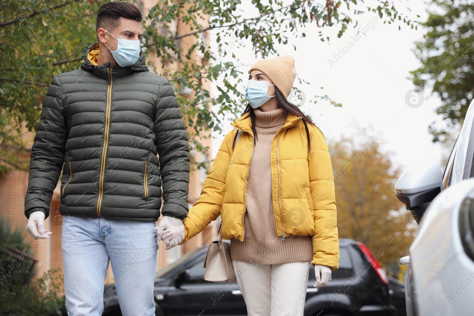 Photo of Couple in medical face masks and gloves walking outdoors. Personal protection during COVID-19 pandemic