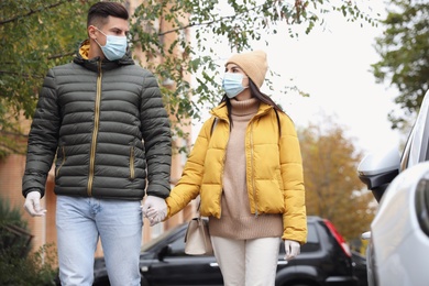 Photo of Couple in medical face masks and gloves walking outdoors. Personal protection during COVID-19 pandemic