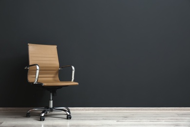 Comfortable office chair near black wall indoors. Space for text