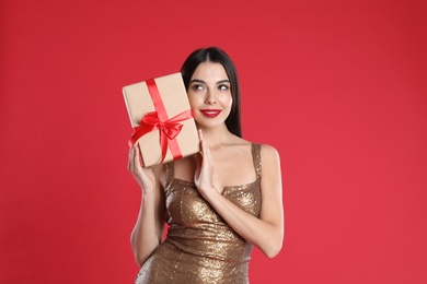 Photo of Woman in golden dress holding Christmas gift on red background