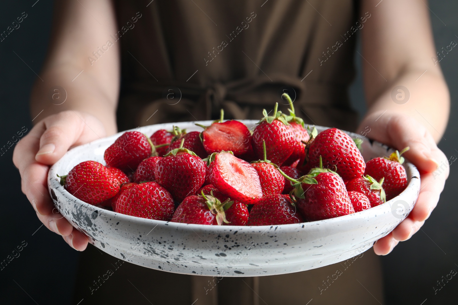 Photo of Woman holding plate with tasty fresh strawberries on black background, closeup