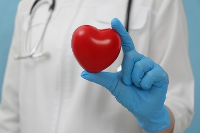 Photo of Doctor holding red heart on light blue background, closeup