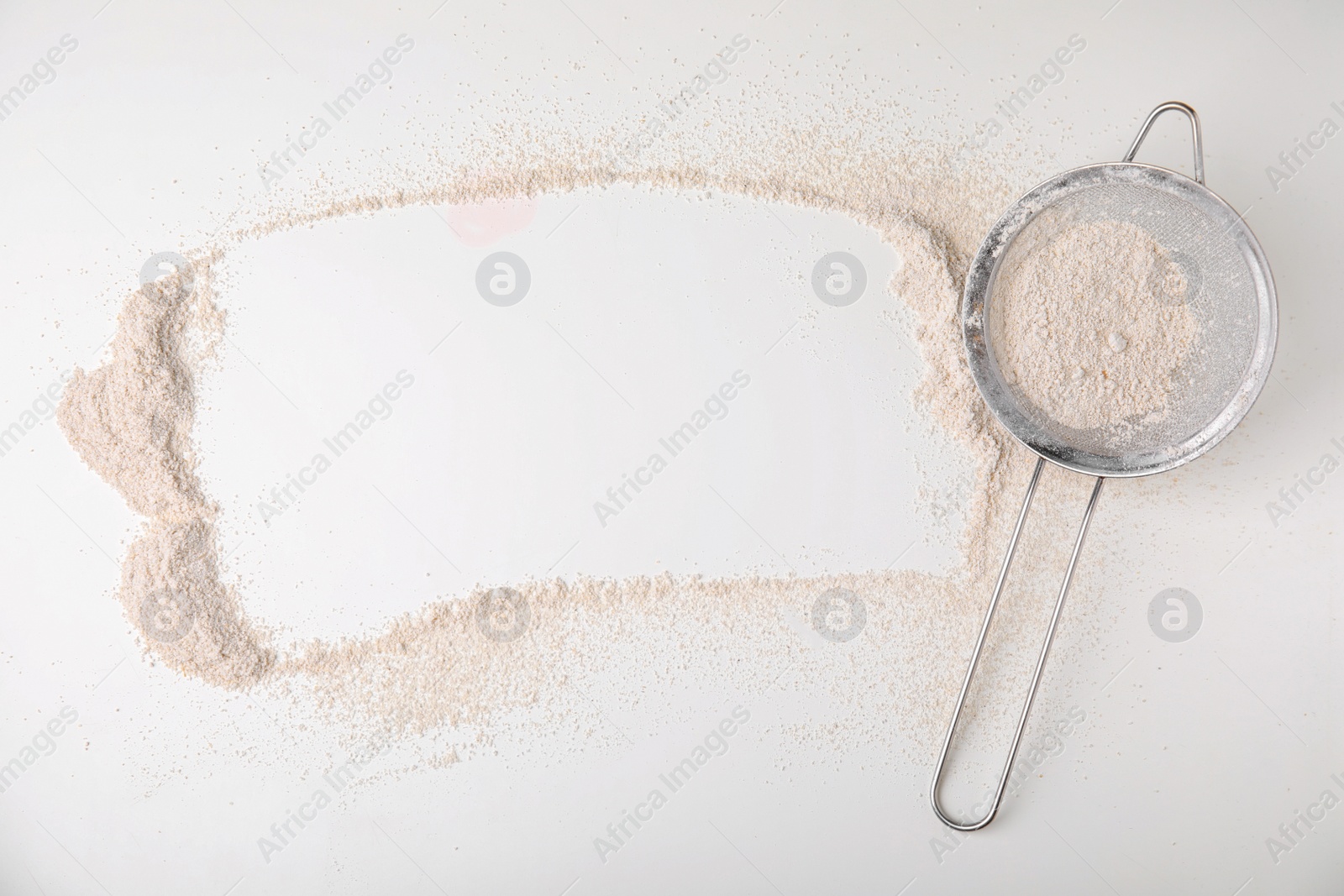 Photo of Frame made of flour and sieve on white table, top view. Space for text