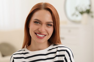 Photo of Portrait of beautiful young woman with red hair at home. Attractive lady smiling and looking into camera