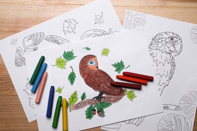 Colored and blank drawings with crayons on wooden table, flat lay