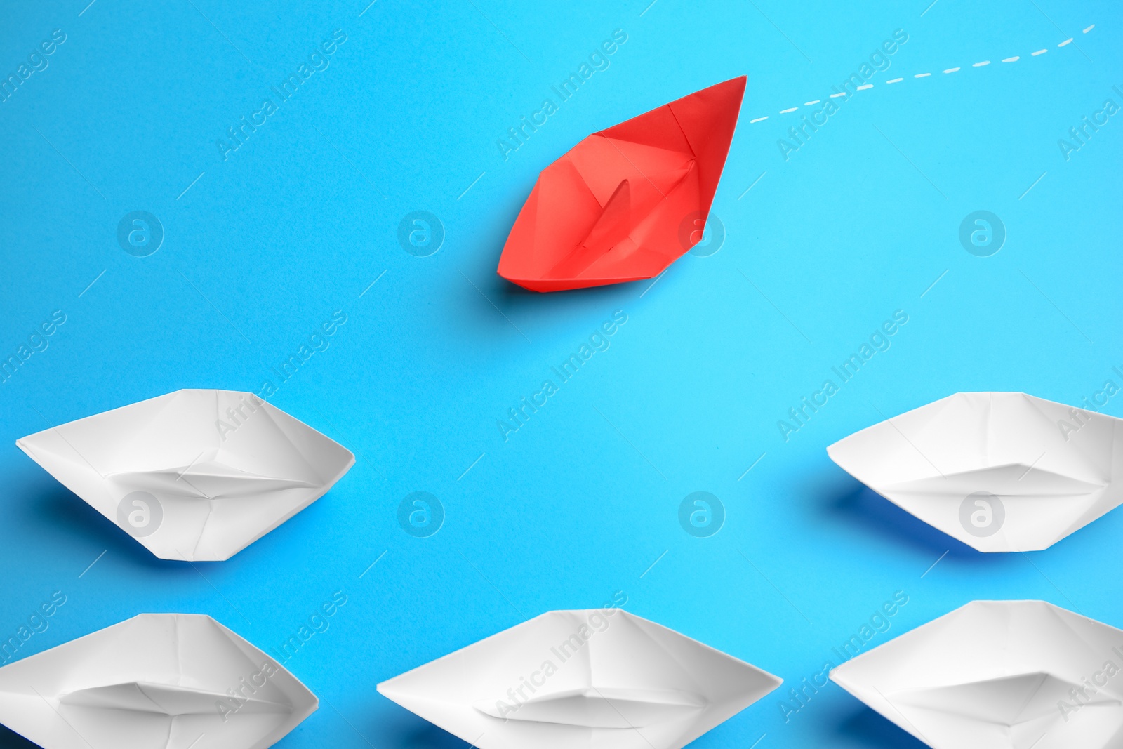 Photo of Red paper boat floating to others on light blue background. Uniqueness concept