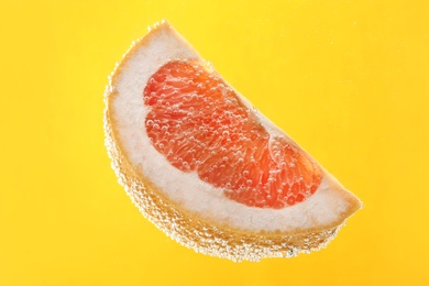 Photo of Slice of grapefruit in sparkling water on yellow background. Citrus soda