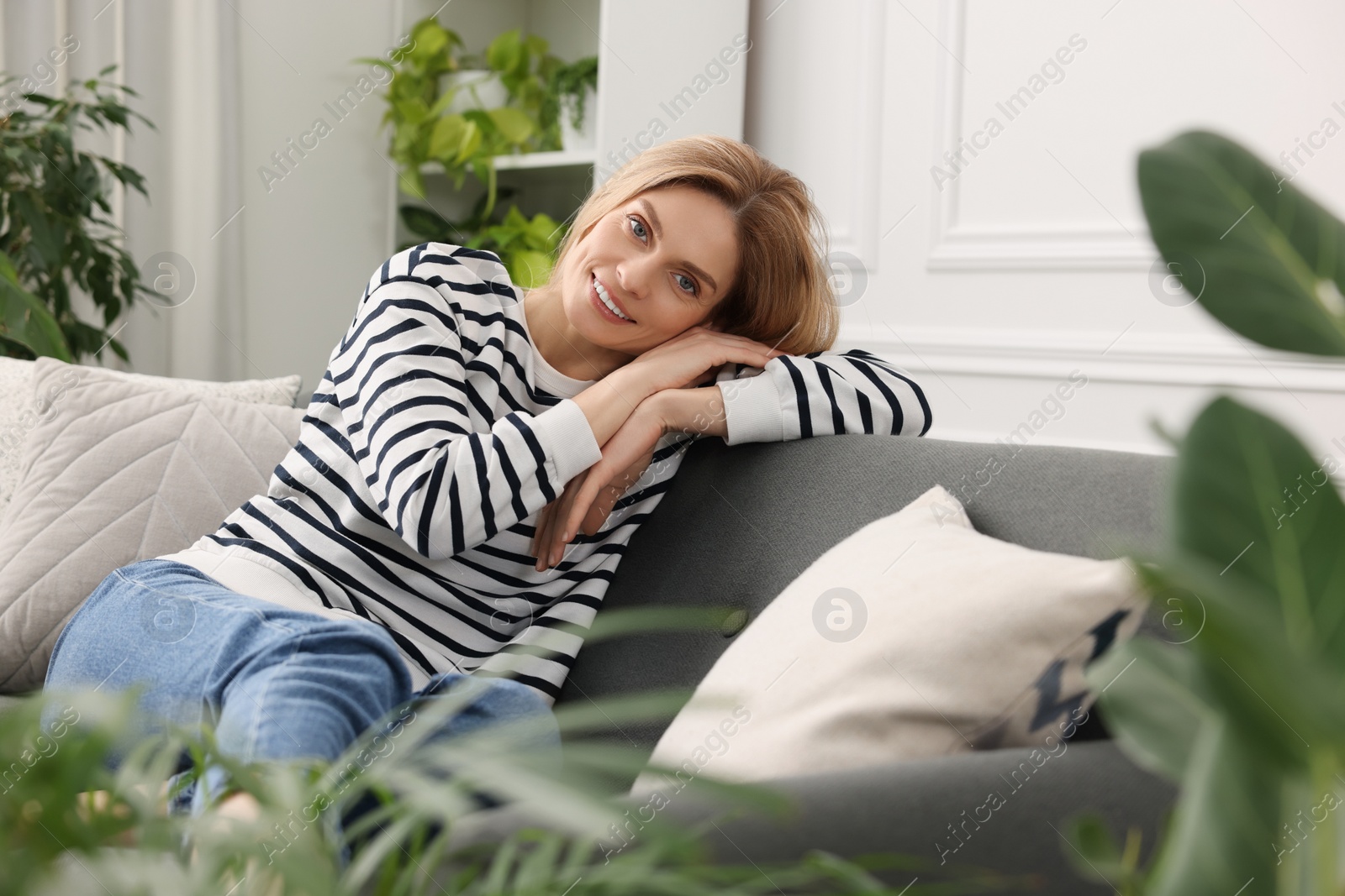 Photo of Woman relaxing on sofa surrounded by beautiful potted houseplants at home