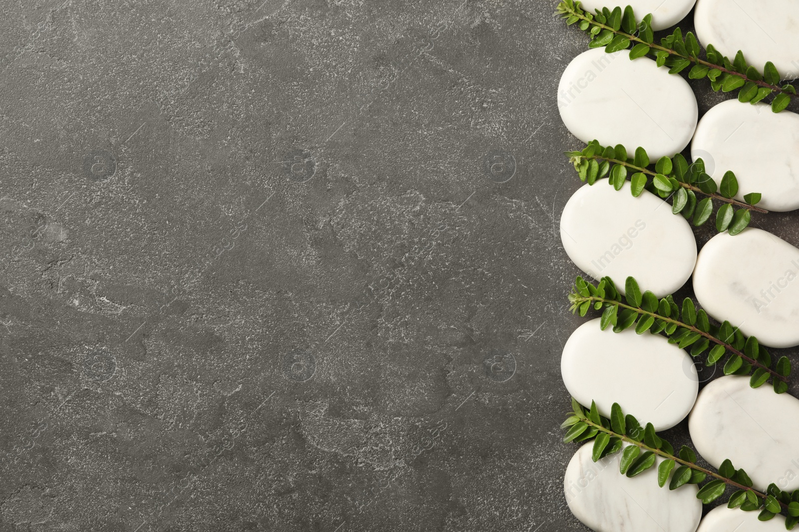 Photo of Spa stones and branches of plant on grey table, flat lay. Space for text