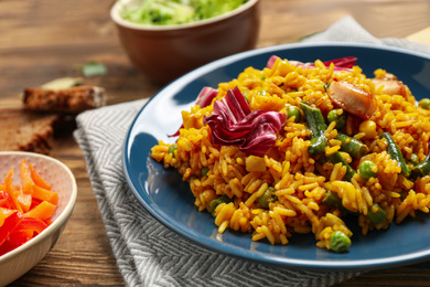 Photo of Delicious rice pilaf with chicken and vegetables on wooden table