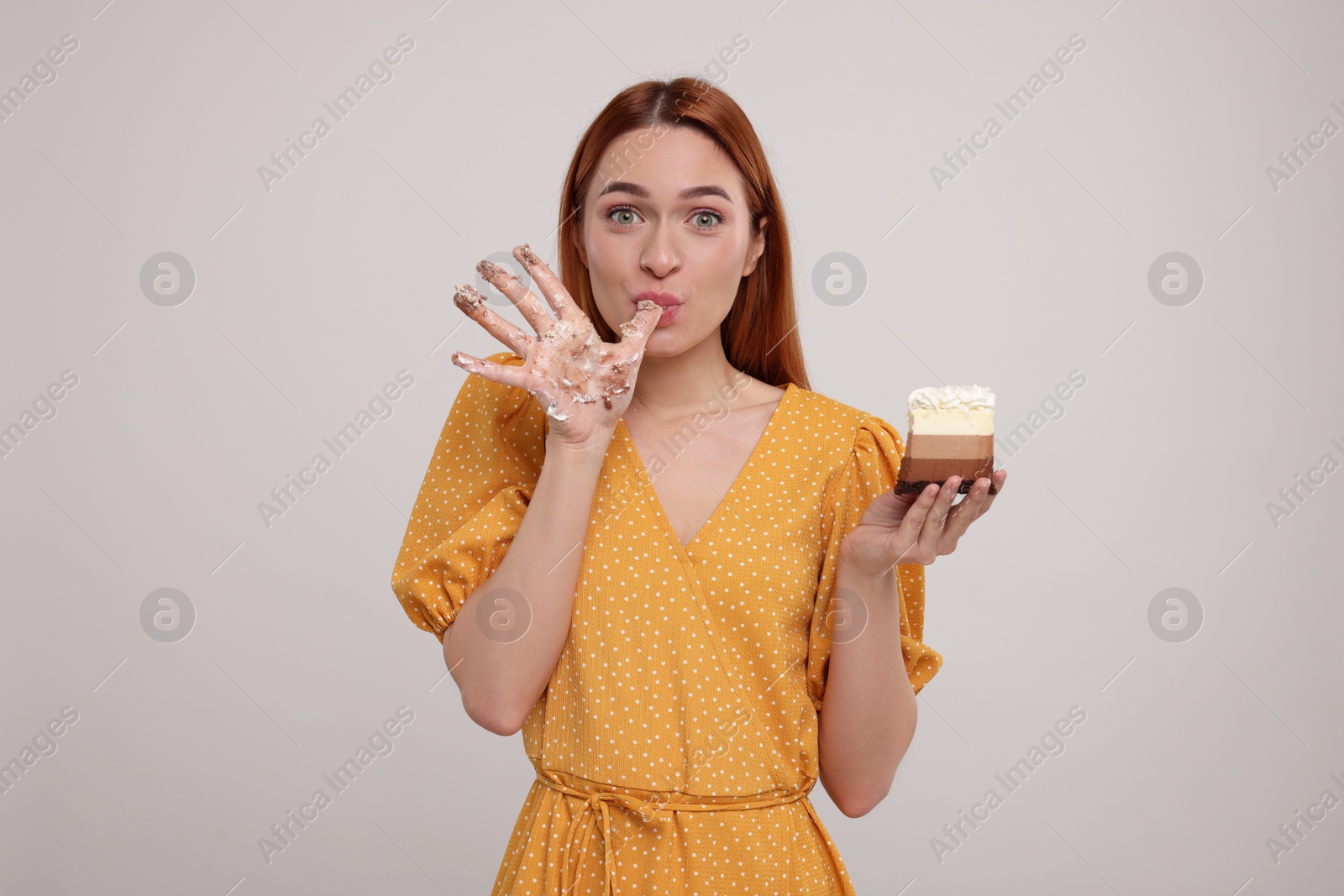 Photo of Young woman eating piece of tasty cake on light grey background