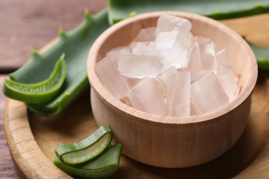 Photo of Aloe vera gel and slices of plant on wooden table, closeup