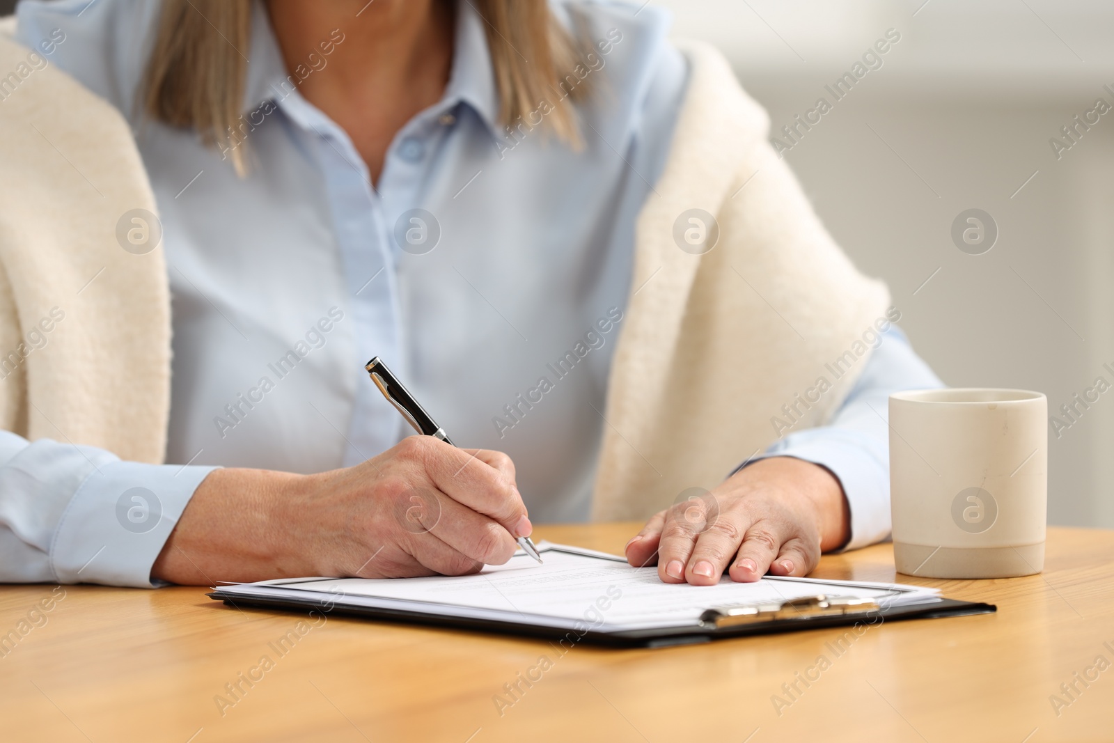 Photo of Senior woman signing Last Will and Testament at table indoors, closeup