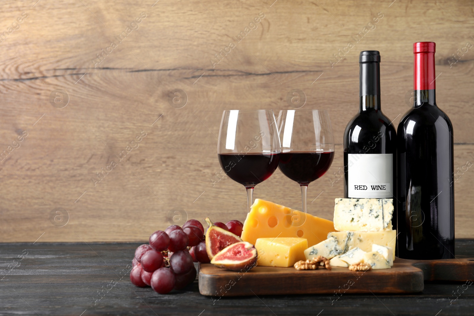 Photo of Different delicious cheeses, fruits and wine on table against wooden background, space for text