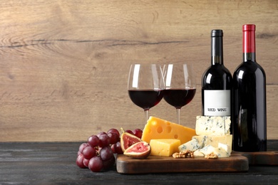 Different delicious cheeses, fruits and wine on table against wooden background, space for text