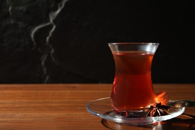 Photo of Glass of traditional Turkish tea on wooden table against black background. Space for text