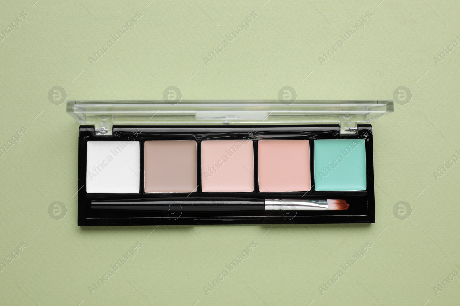 Photo of Colorful contouring palette with brush on pale green background, top view. Professional cosmetic product