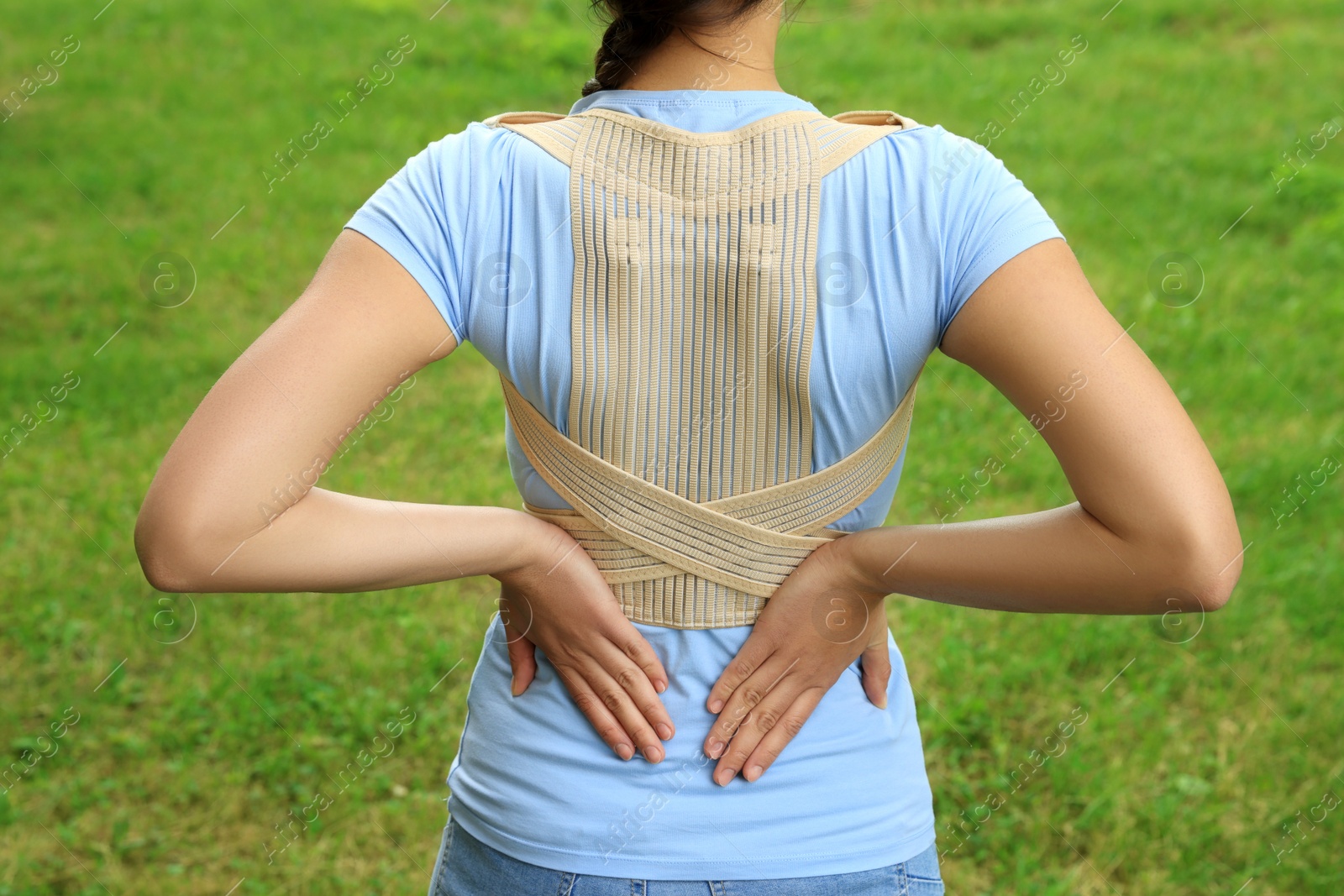 Photo of Closeup of woman with orthopedic corset on green grass outdoors, back view