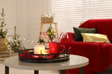 Photo of Candles and red cup with candy canes on white table in decorated room. Christmas interior design