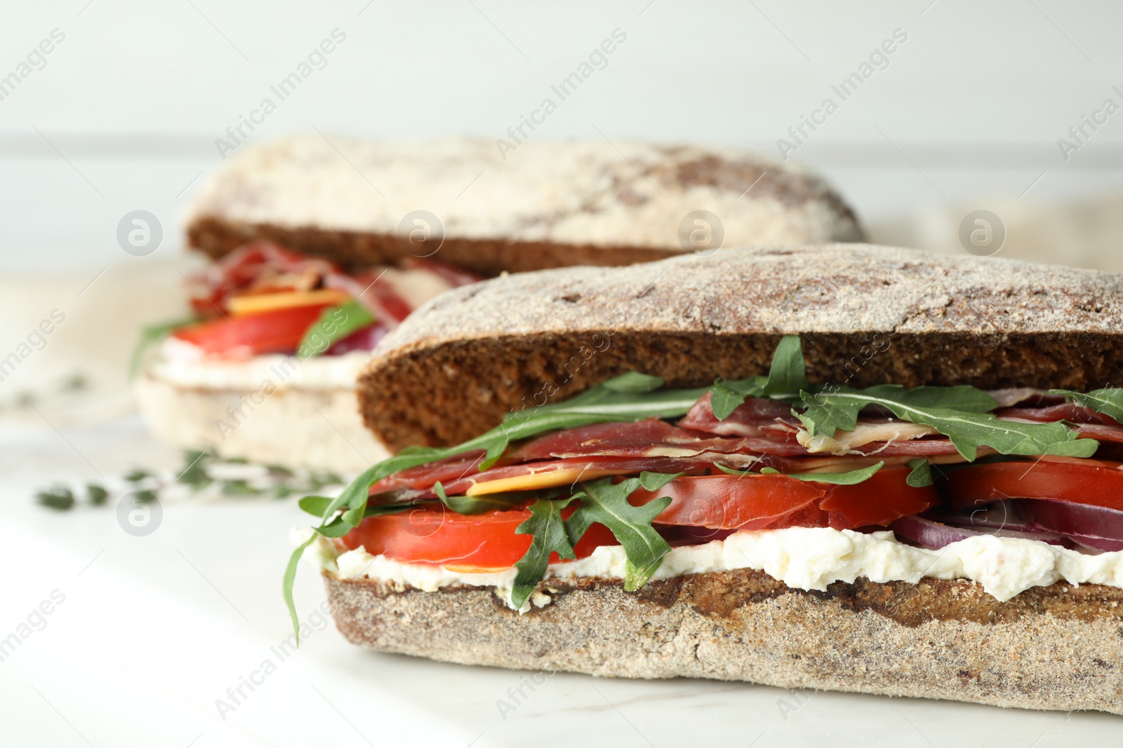 Photo of Delicious sandwiches with fresh vegetables and prosciutto on white table, closeup