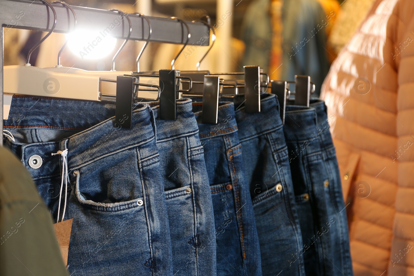 Photo of Modern jeans hanging on clothing rack in shop, closeup