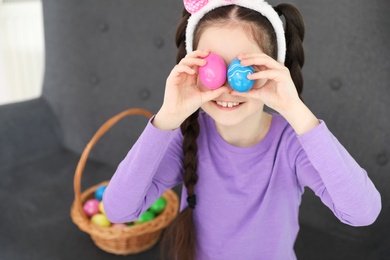 Photo of Little girl holding Easter eggs near eyes at home