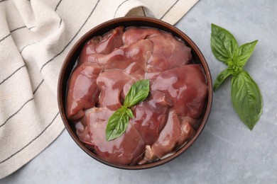 Photo of Bowl with raw chicken liver and basil on light grey table, flat lay