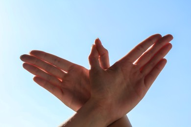 Woman making hand gesture like bird on light blue background, closeup