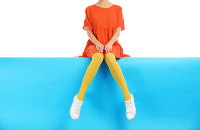Woman wearing yellow tights and stylish shoes sitting on color background, closeup