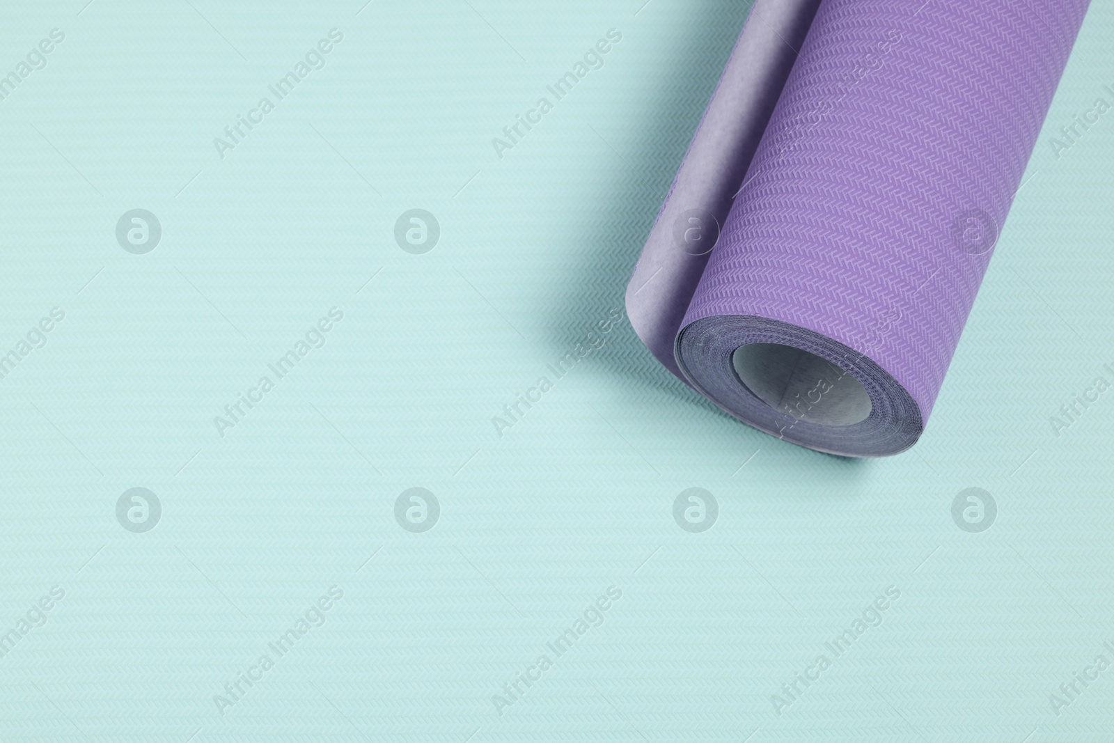 Photo of One violet wallpaper roll on light turquoise sample, top view. Space for text