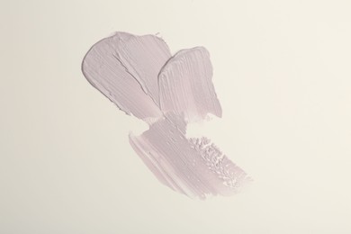 Strokes of purple color correcting concealers on white background, top view