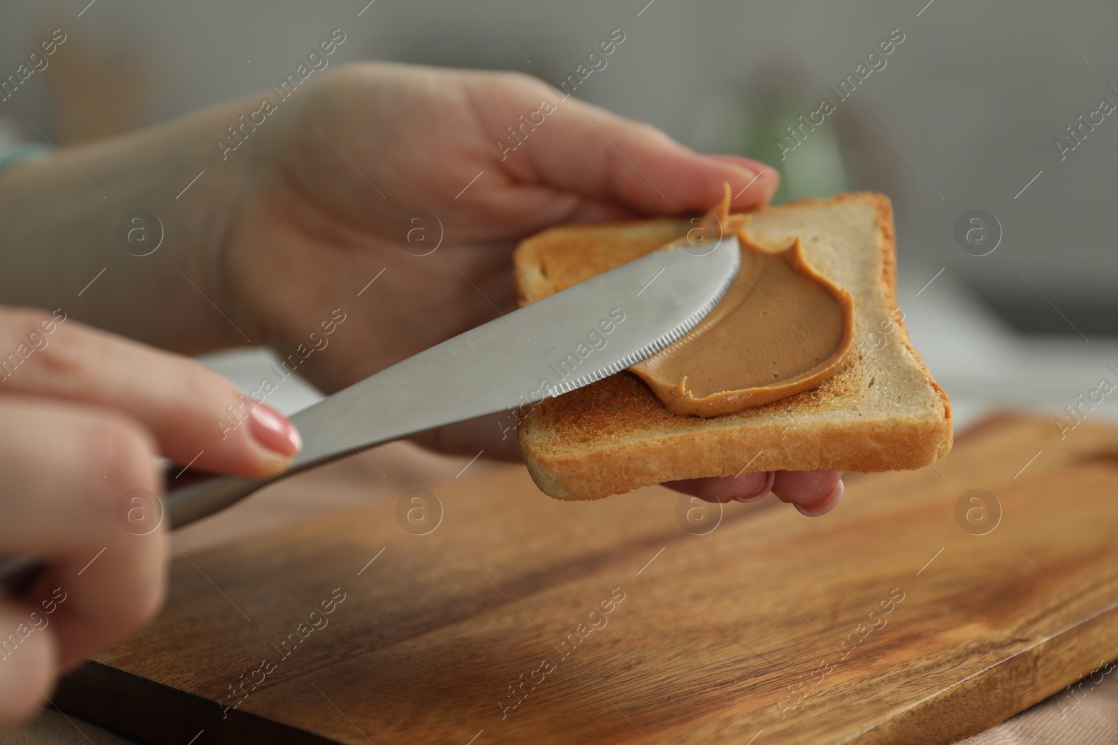 Photo of Woman spreading tasty nut butter onto toast at table, closeup