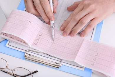 Doctor examining cardiogram at table in clinic, closeup