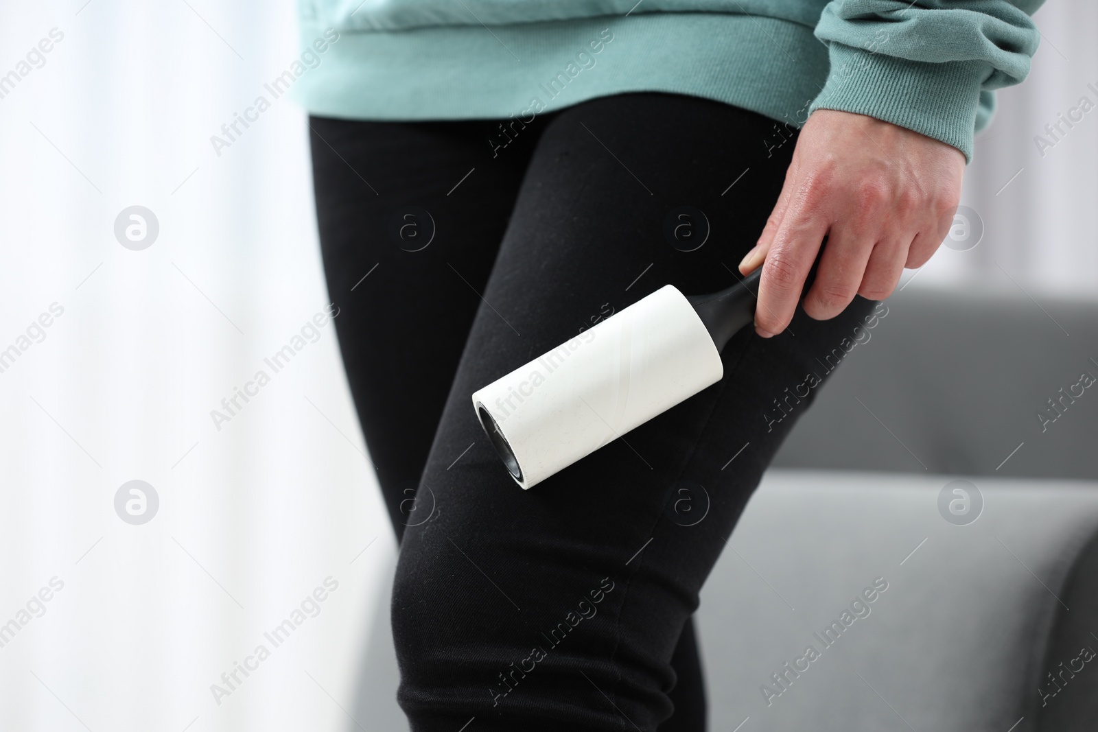 Photo of Woman with lint roller removing pet hair from black trousers indoors, closeup