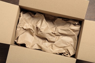 Open cardboard box with crumpled paper on wooden floor, top view. Packaging goods