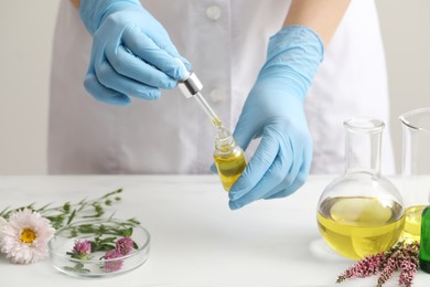 Photo of Scientist developing cosmetic oil at white table, closeup