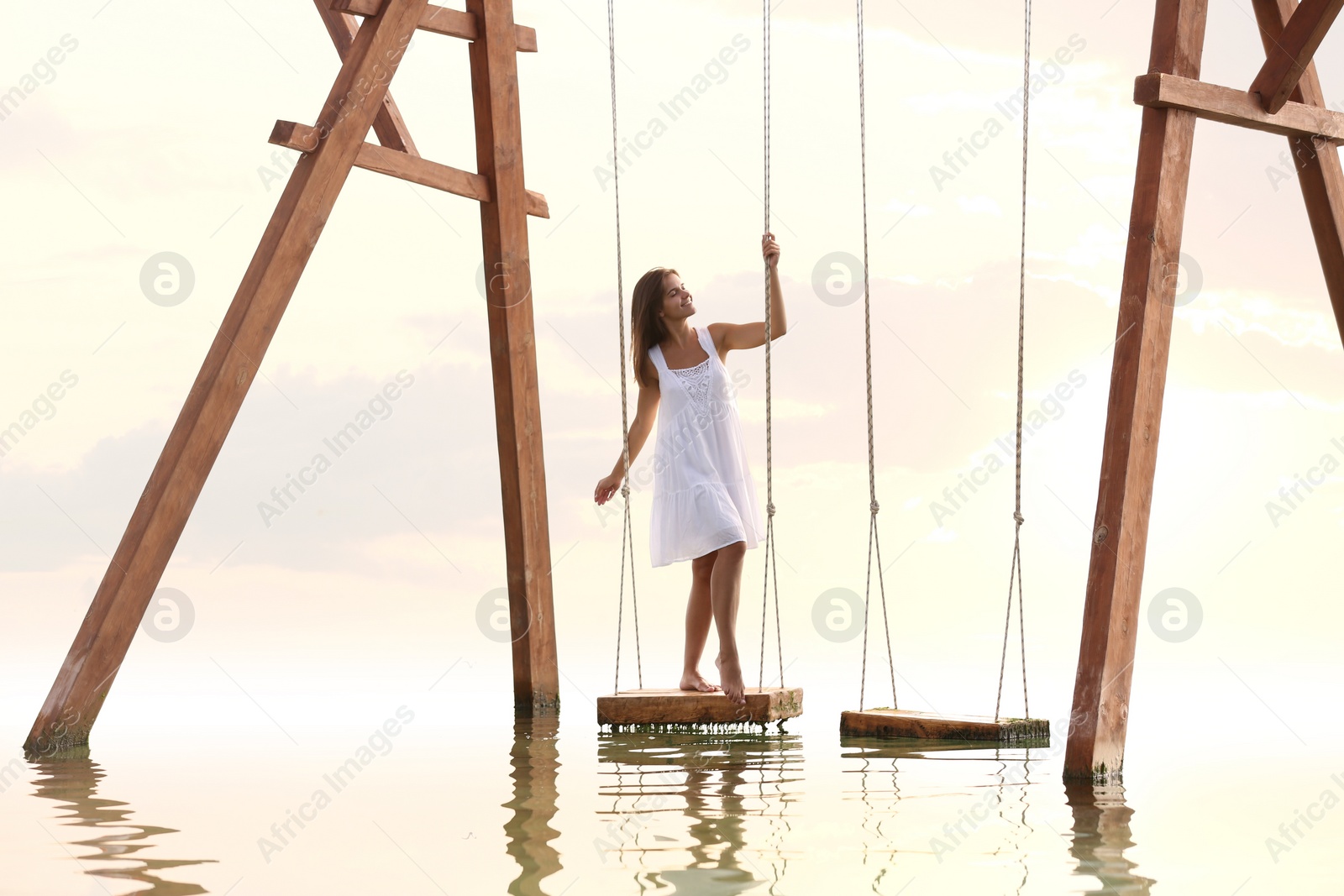 Photo of Young woman enjoying sunrise on swing over water