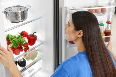 Young woman near modern refrigerator indoors, back view