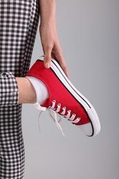 Photo of Woman putting on red classic old school sneaker against light grey background, closeup