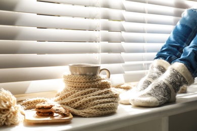 Photo of Woman and cup of hot winter drink near window indoors, closeup