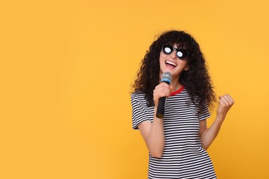 Photo of Beautiful young woman with microphone and sunglasses singing on yellow background. Space for text