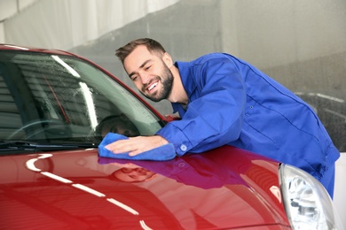 Photo of Worker cleaning automobile bonnet with rag at car wash