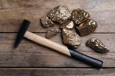 Pile of gold nuggets and hammer on wooden table, flat lay