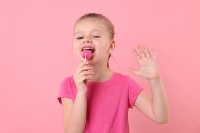 Photo of Cute little girl licking lollipop on pink background