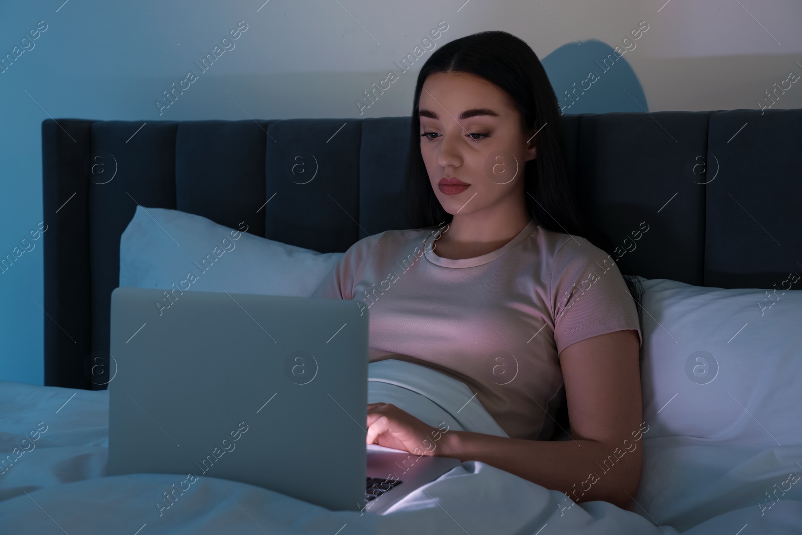 Photo of Young woman using laptop in bed at night. Internet addiction