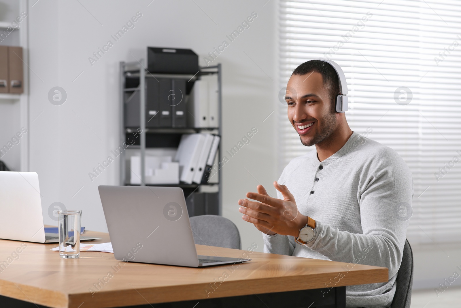Photo of Young man with headphones having video chat via laptop at table in office