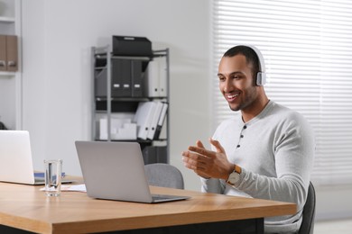 Young man with headphones having video chat via laptop at table in office