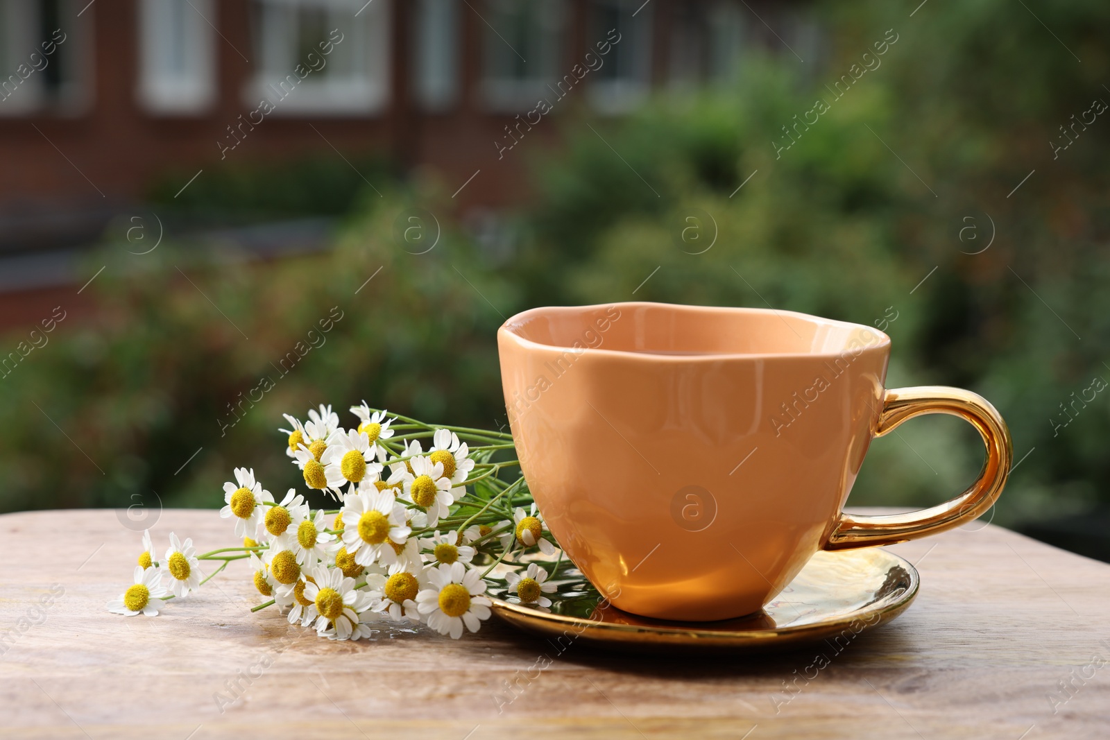 Photo of Cup of delicious chamomile tea and fresh flowers outdoors