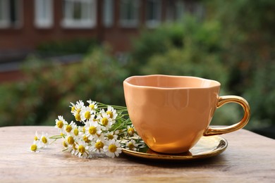 Cup of delicious chamomile tea and fresh flowers outdoors