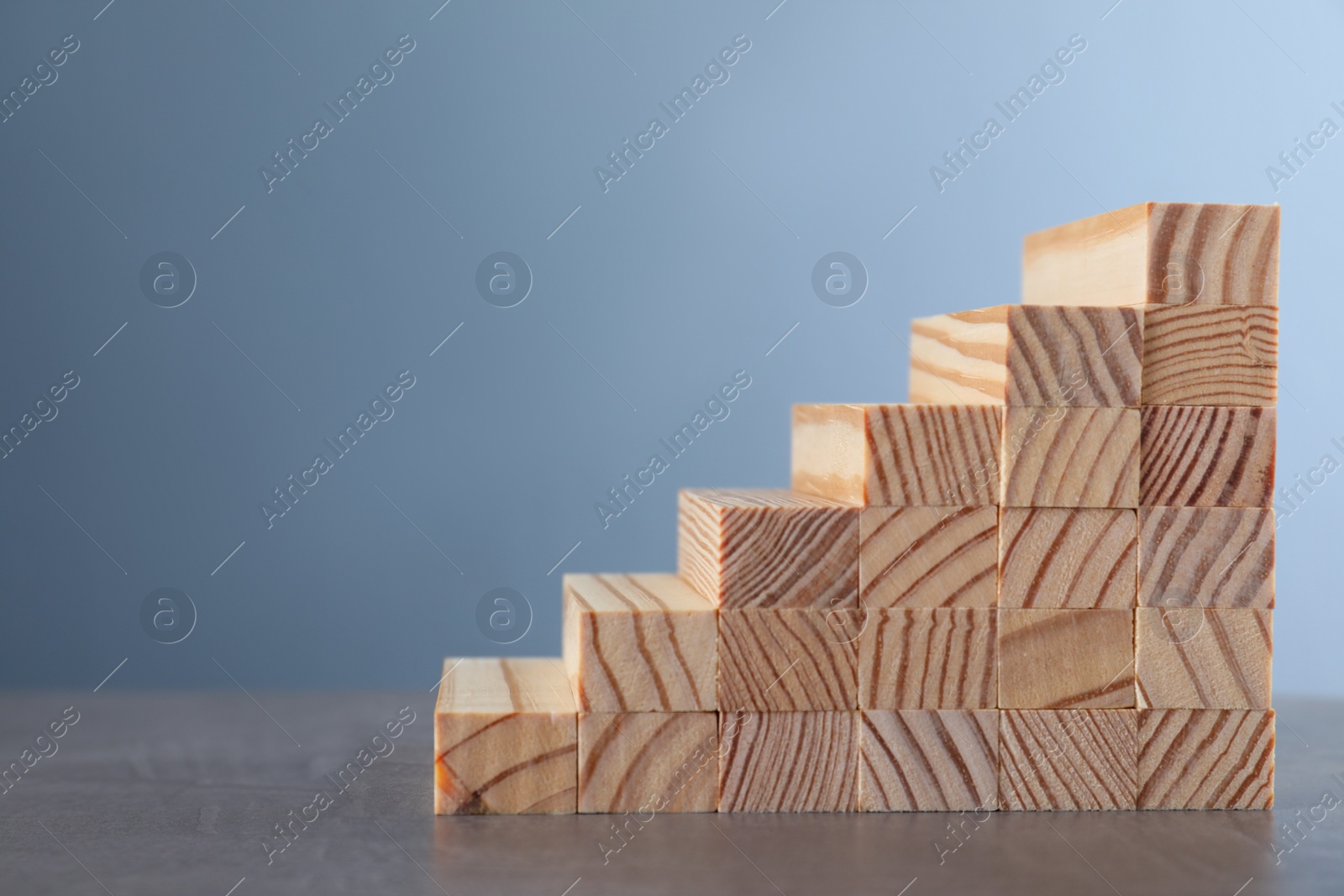 Photo of Steps made with wooden blocks on grey table, space for text. Career ladder